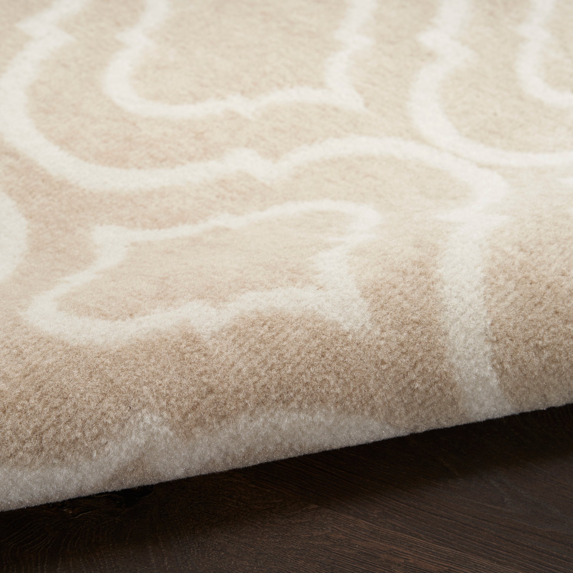 Cream-beige rug with white abstract pattern and soft plush texture on dark wood floor.