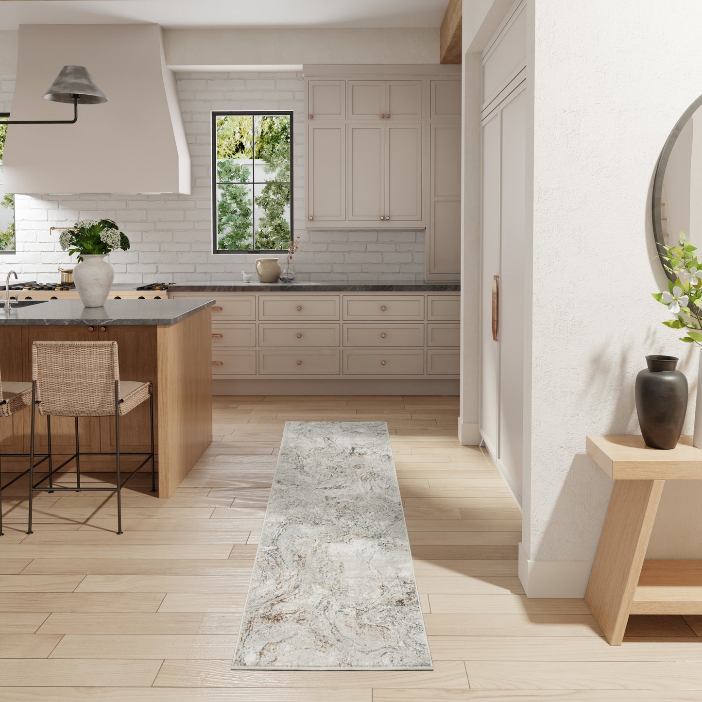 Bright white kitchen with light wood floor, island, white shaker cabinets, gray stone counter, metal bar stools, runner rug.