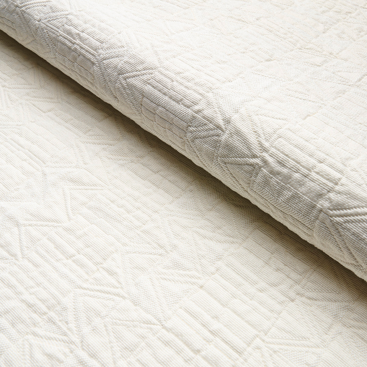 Cream quilted blanket with geometric stitched pattern and folded edge, soft textured bedding fabric.