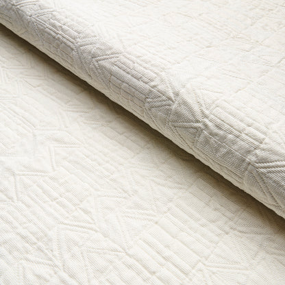 Cream quilted blanket with geometric stitched pattern and folded edge, soft textured bedding fabric.