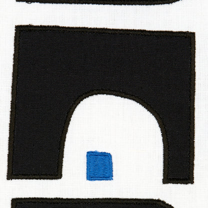 Black arch-shaped embroidered patch with brown edge on white fabric; small blue square inside the arch opening.