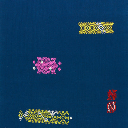 Blue textile with yellow diamond top-right, pink diamond cluster center-left, yellow-white zigzag bottom-left, red emblem right