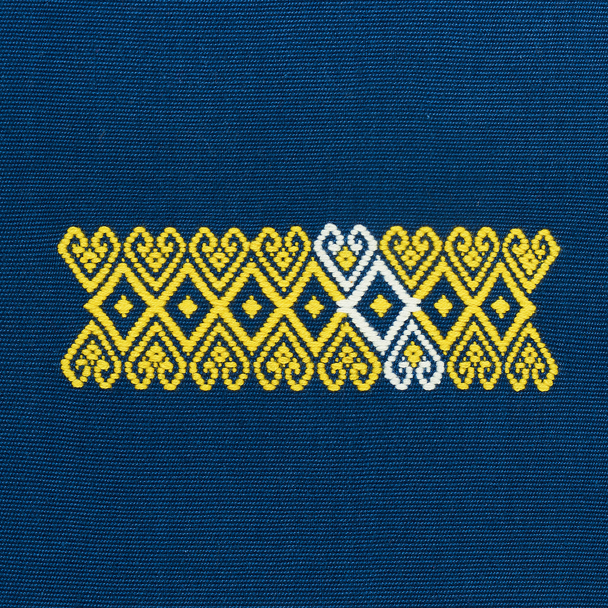 Yellow and white geometric embroidery band with diamond motifs on blue denim fabric.