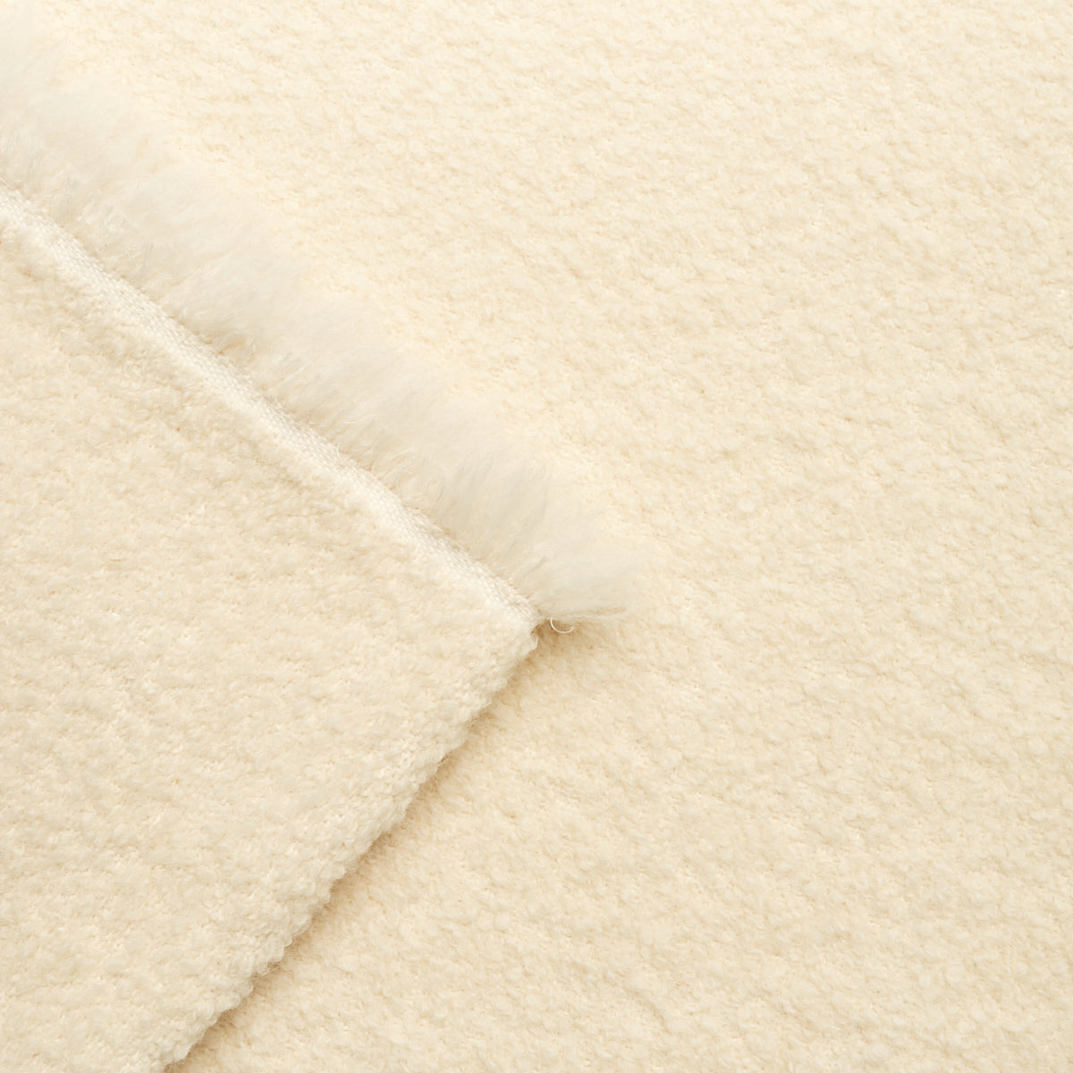 Cream plush blanket & fluffy fringe along folded edge, soft wooly texture.
