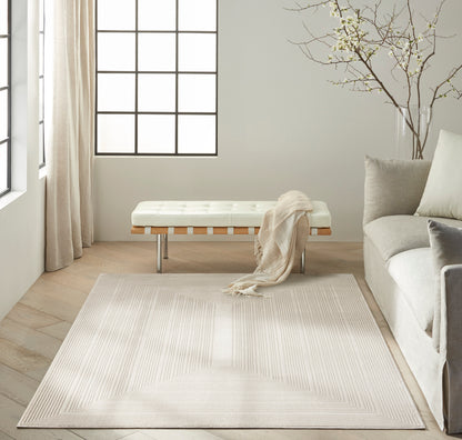 Neutral living room with tufted white bench, beige throw, pale rug, gray sofa, bare tree branches, and large grid-window.