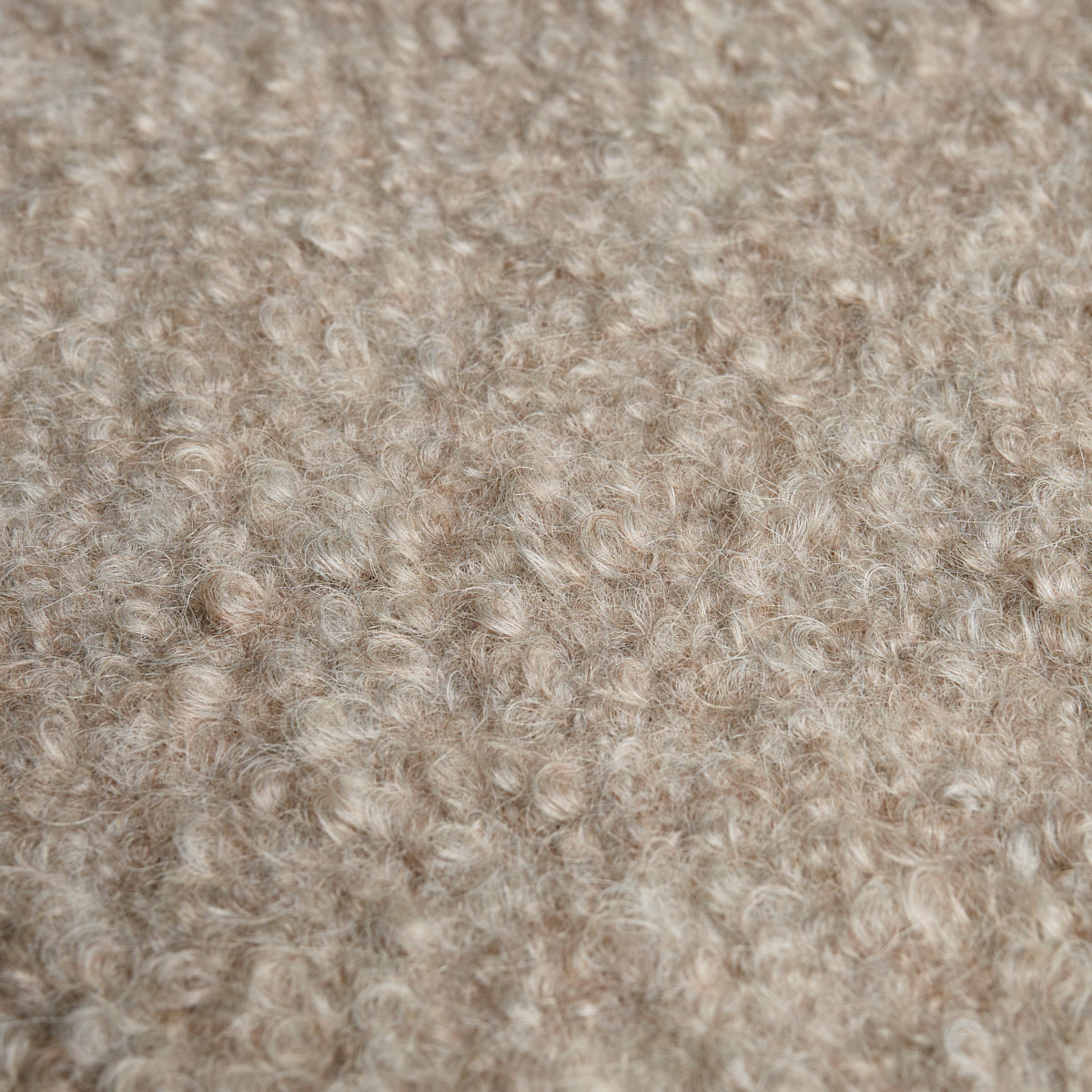 Beige boucle wool fabric close-up with soft curly fibers and cozy textured surface.