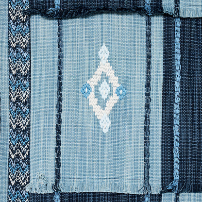 Blue woven rug with vertical stripes, central light-blue field with white diamond motif, dark blue borders and fringed edges.