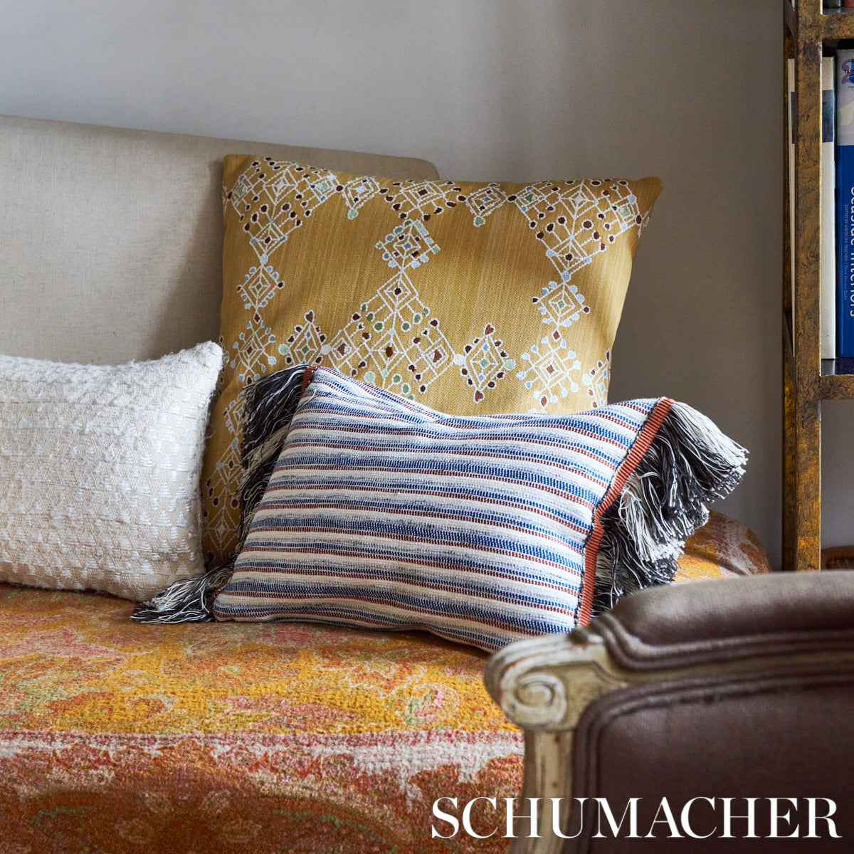 Yellow-gold pillow with white lattice, white textured pillow, and blue striped fringe pillow on an orange patterned sofa.