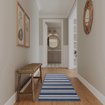 Coastal hallway with pale green walls, wooden bench, blue striped runner, and wicker round mirror near bathroom.