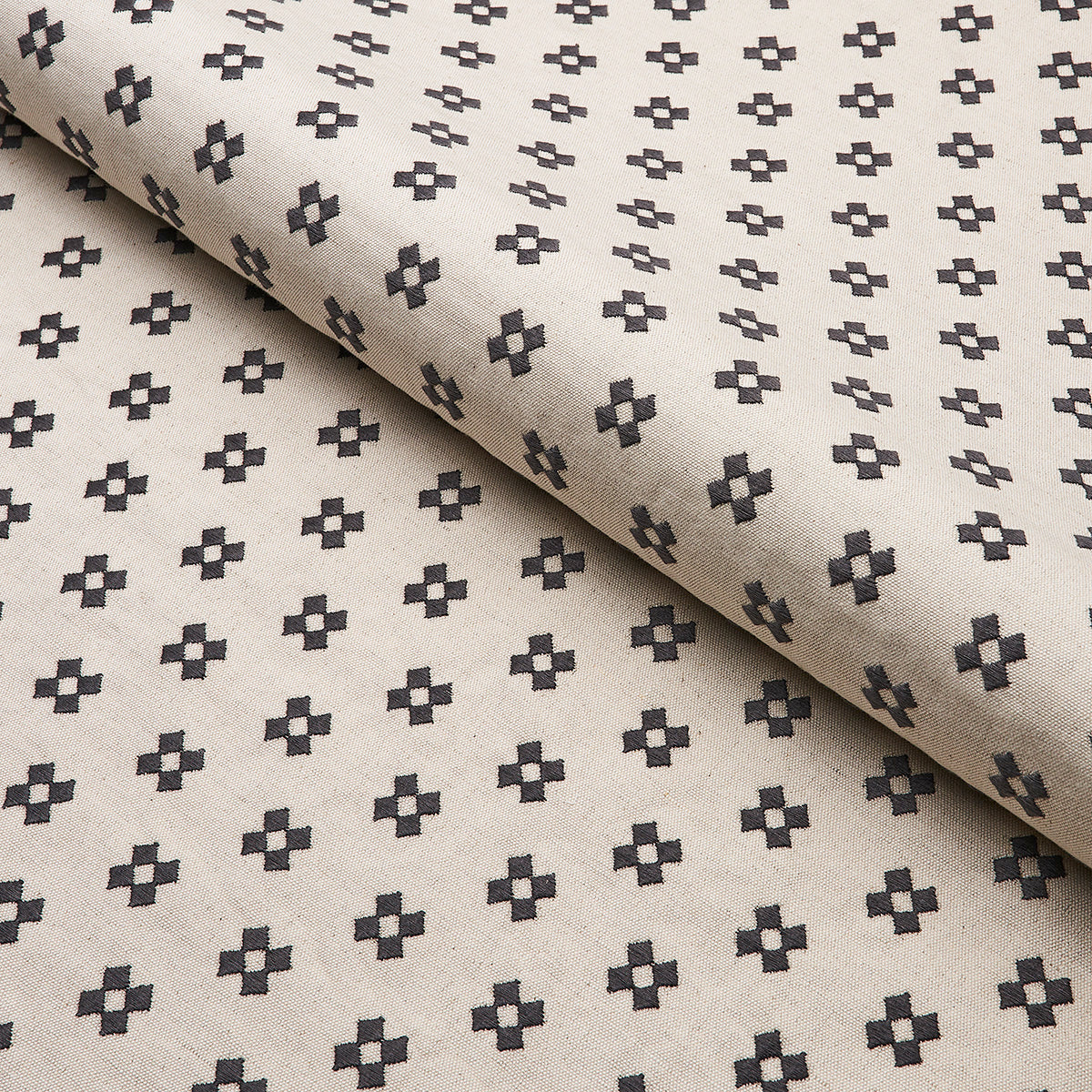 Beige fabric with repeating small dark cross motifs; rolled edge, lightweight geometric textile.