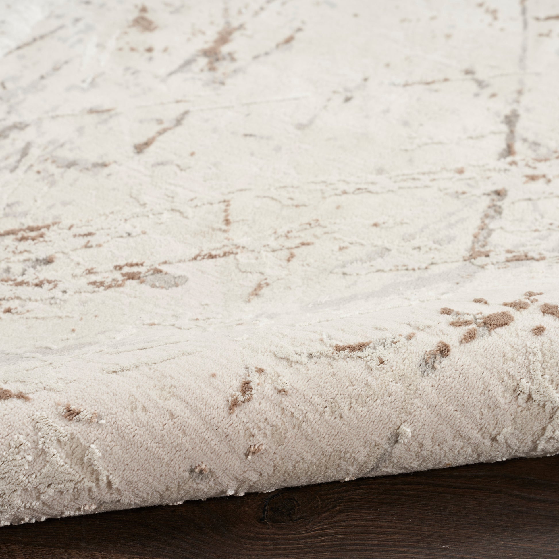 Cream plush rug with a subtle brown abstract pattern placed on dark wood floor.