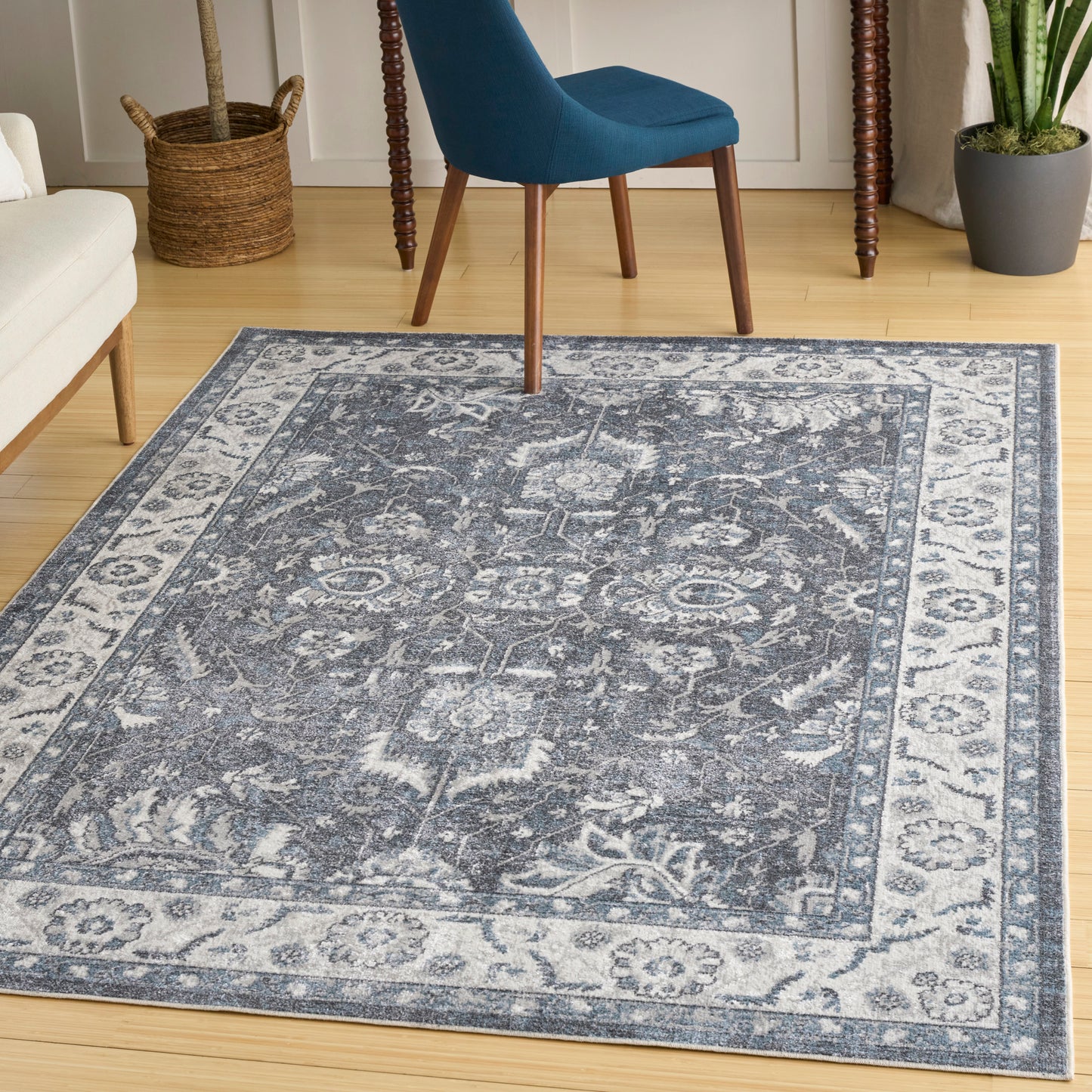 Blue-gray oriental area rug with faded pattern and light border on wooden floor, beside a blue chair.
