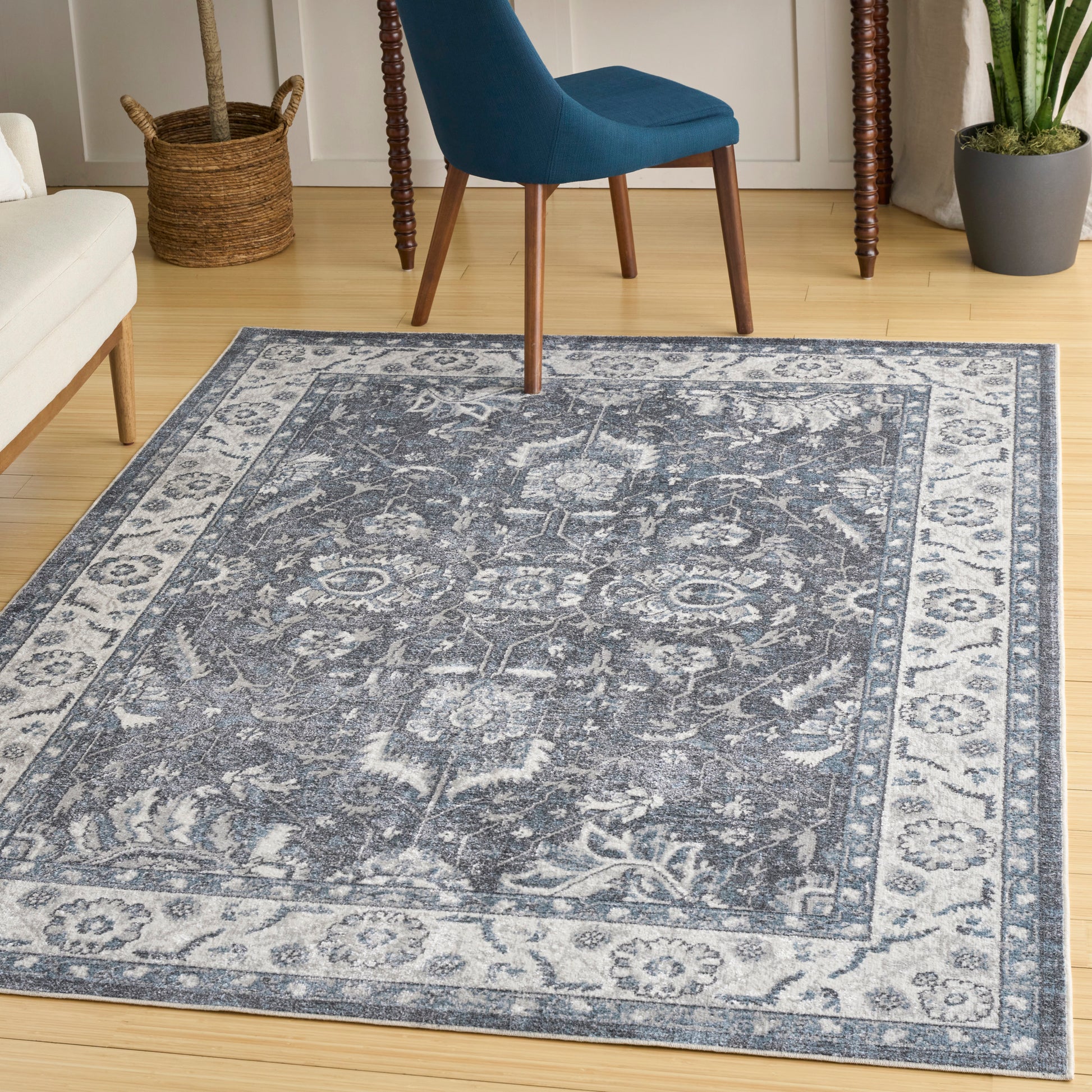 Blue-gray oriental area rug with faded pattern and light border on wooden floor, beside a blue chair.