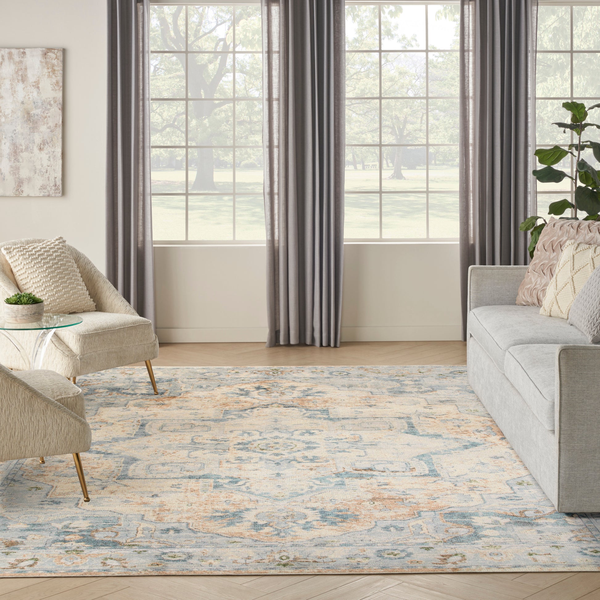 Bright living room with gray sofa, beige lounge chair, glass side table, & blue-beige patterned rug.