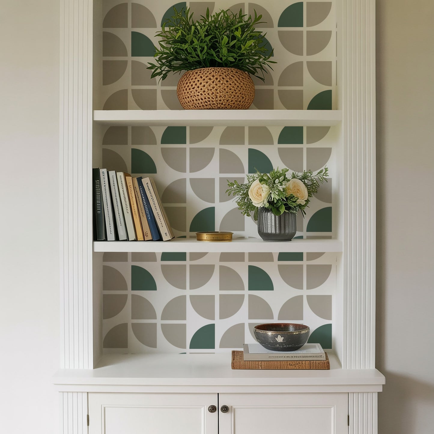 White built-in shelf with geometric wallpaper; top plant in woven basket, middle books and floral vase, bottom bowl on books.