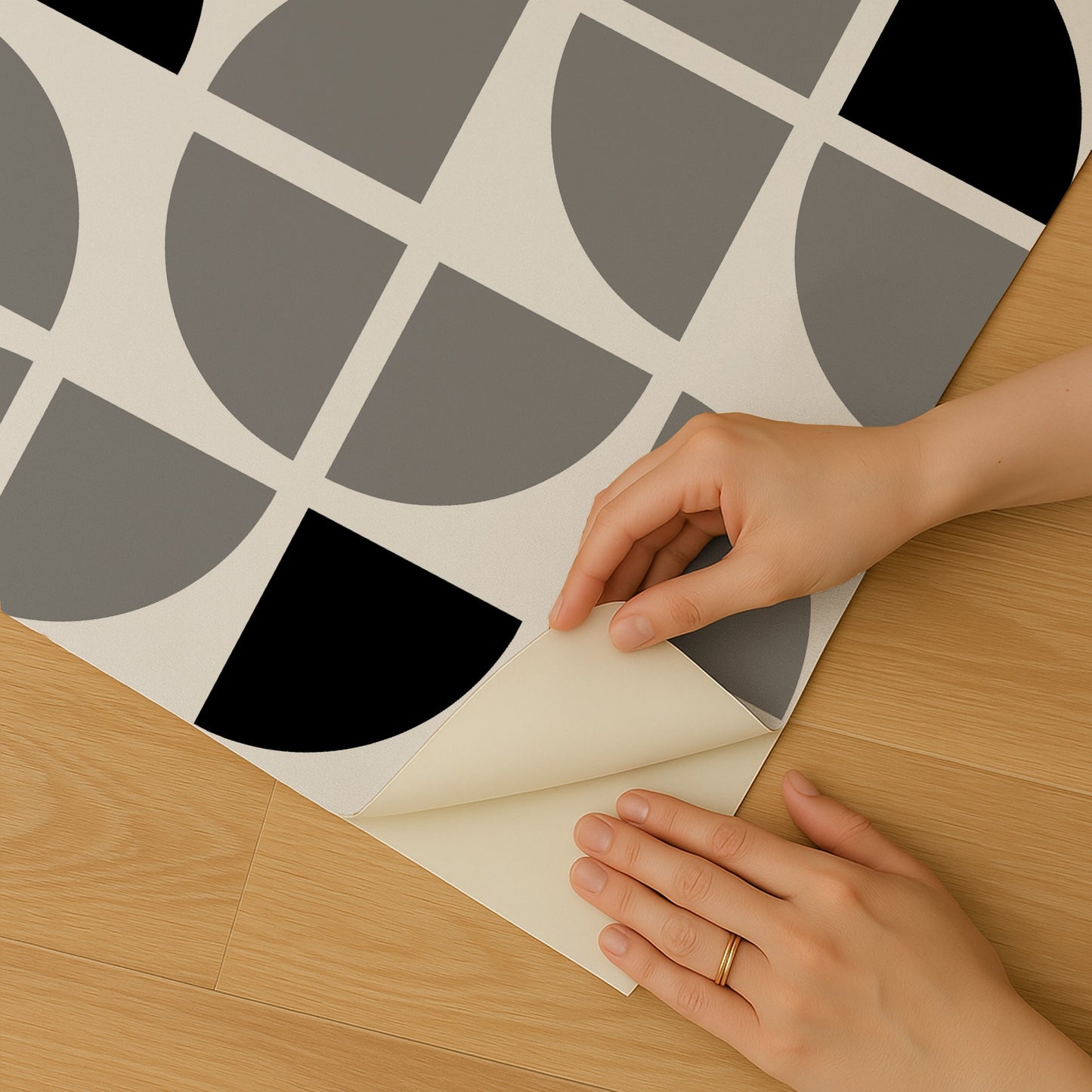 Geometric grayscale wallpaper sample with circle/quarter patterns peeled back on a wooden floor.