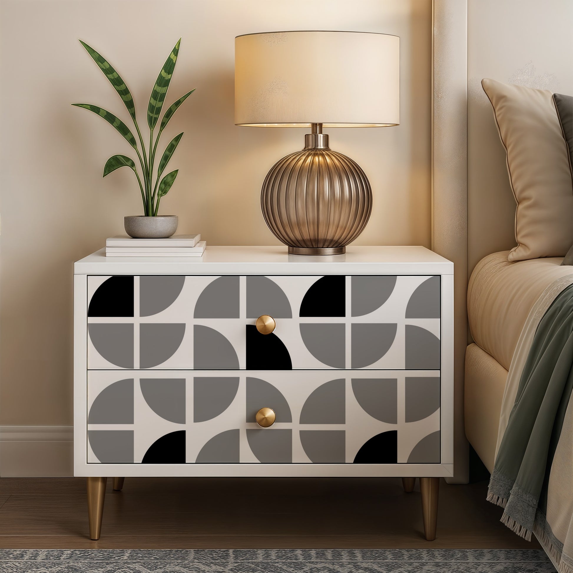 White mid-century nightstand with two-drawer grey arc-pattern fronts, brass knobs, gold legs; lamp and plant on top.