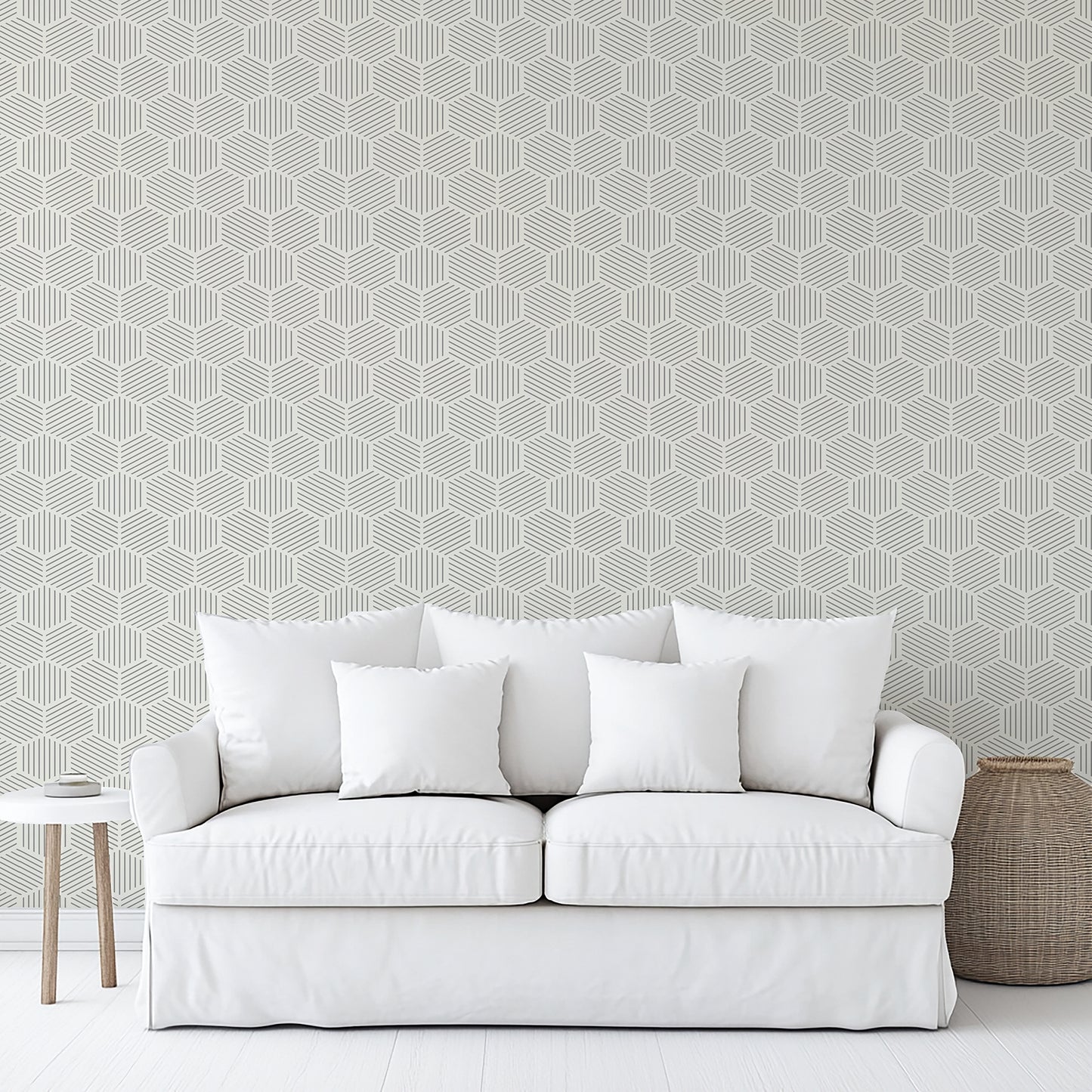 Gray striped hexagonal mosaic peel-and-stick wallpaper on the wall in a minimalist room; a white slipcovered sofa with cushions and a side table are visible.