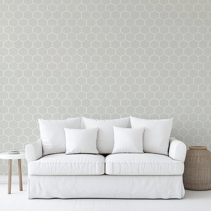 Gray striped hexagonal mosaic peel-and-stick wallpaper on the wall in a minimalist room; a white slipcovered sofa with cushions and a side table are visible.