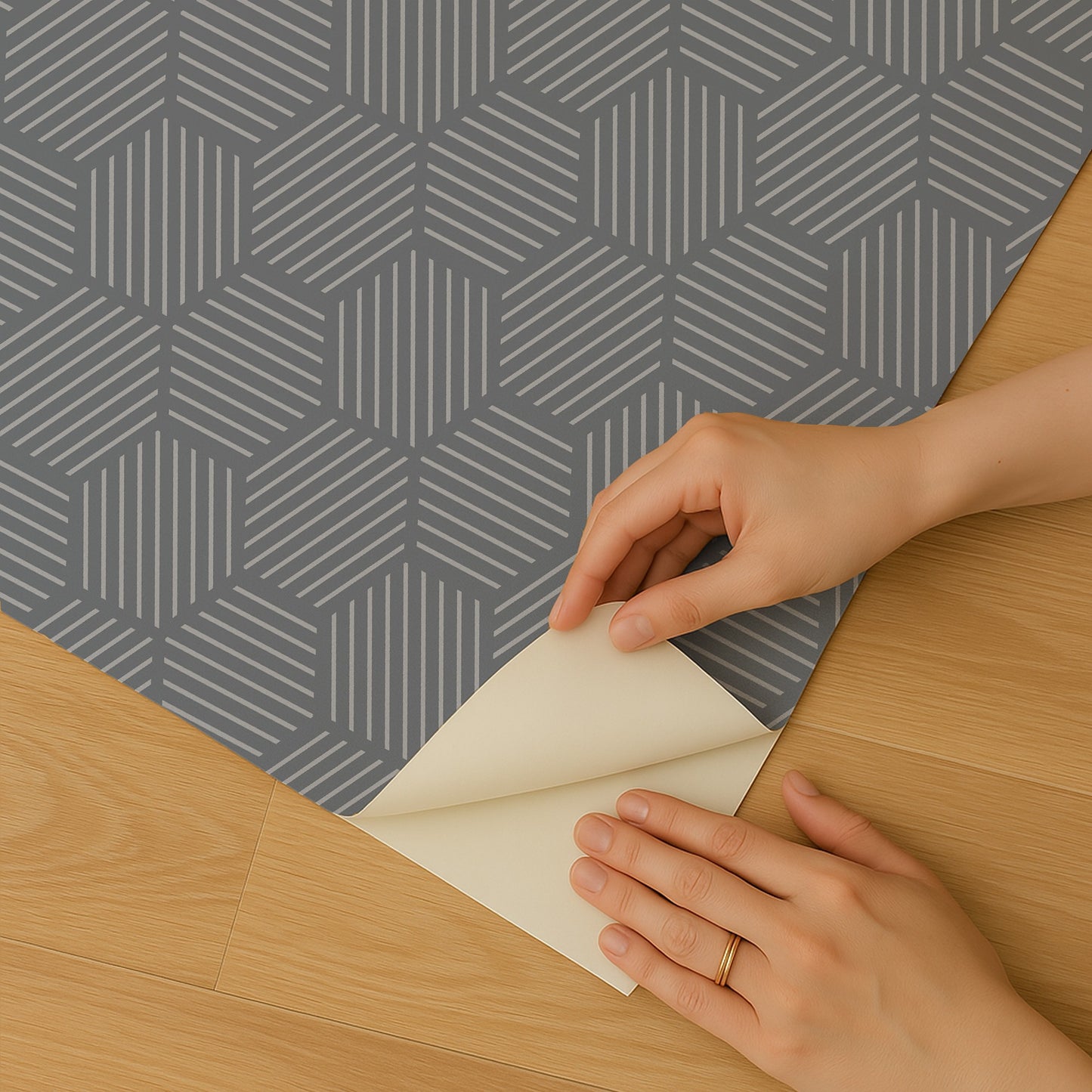 Blue peel-and-stick wallpaper with a striped hexagonal mosaic pattern being peeled back by hands on a wooden floor
