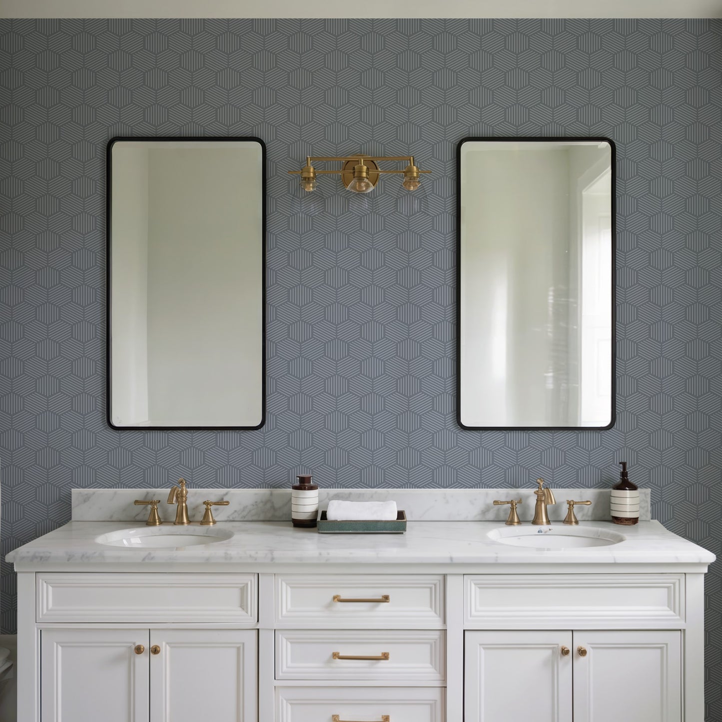 Double-sink white vanity with marble top, gold faucets, two black-framed mirrors, blue hex wallpaper, brass wall light.