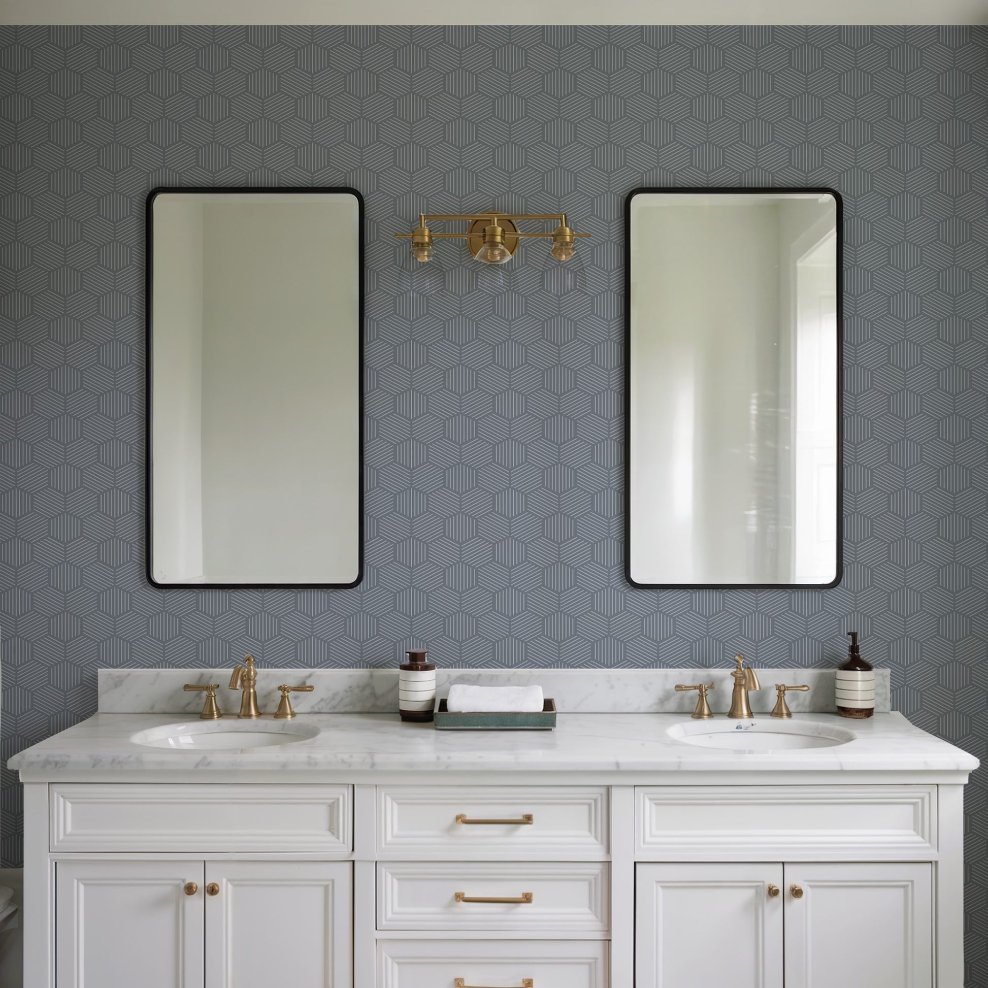 Double-sink white vanity with marble top, gold faucets, two black-framed mirrors, blue hex wallpaper, brass wall light.