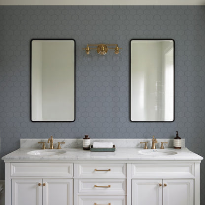 Double-sink white vanity with marble top, gold faucets, two black-framed mirrors, blue hex wallpaper, brass wall light.