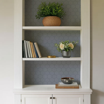 White built-in bookcase with geometric gray wallpaper; top woven plant basket, middle books and cream rose vase, bottom bowl on books.