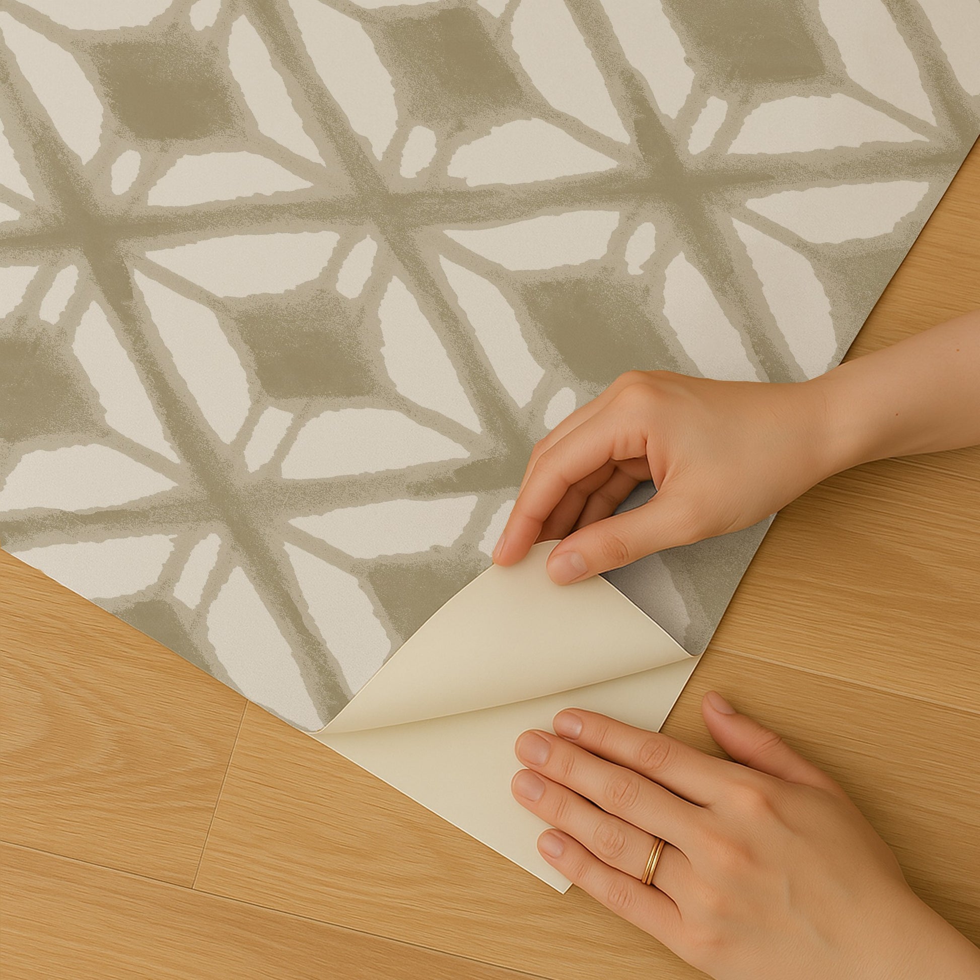 Beige-taupe geometric peel-and-stick wallpaper being peeled back at a corner; hands visible.