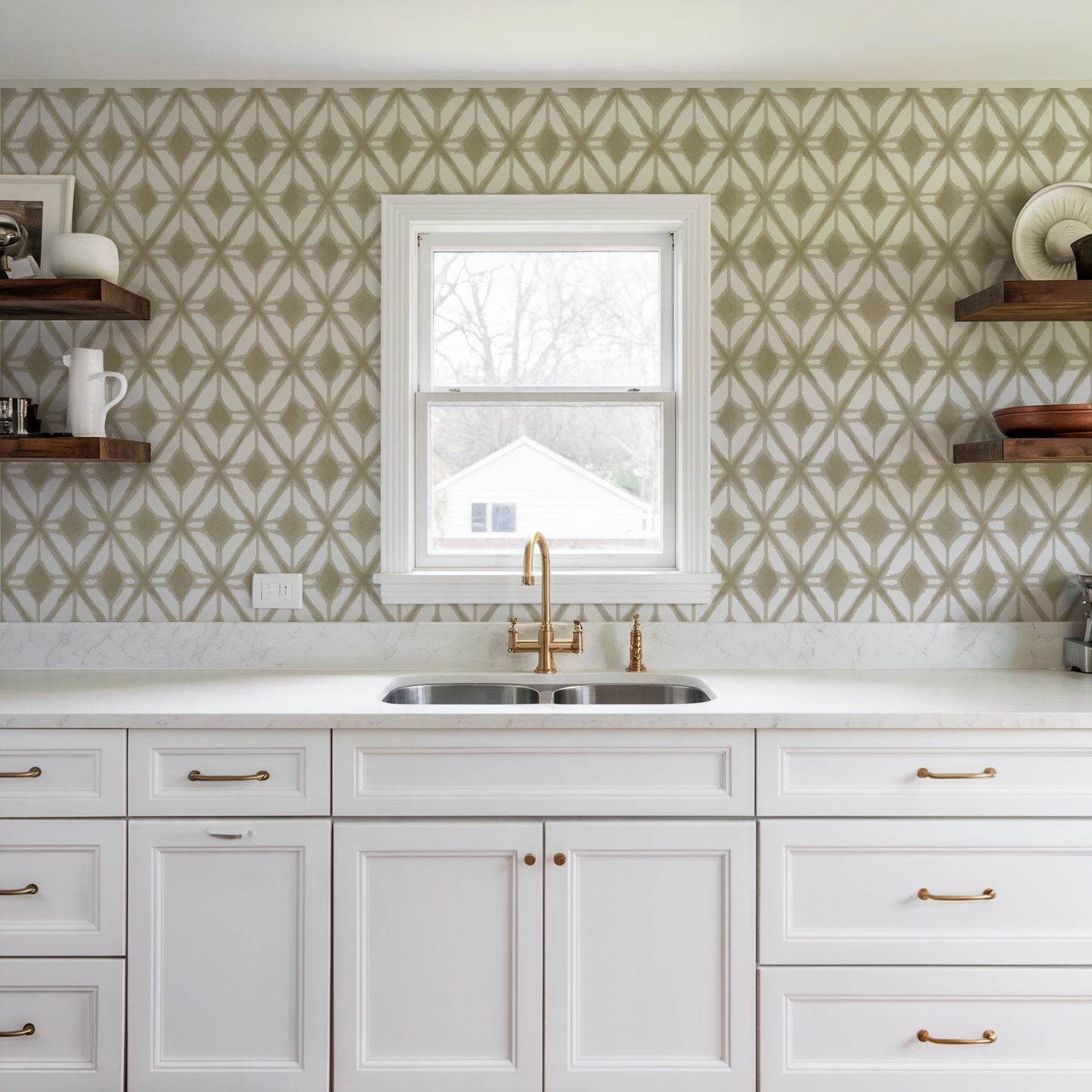 Bright kitchen with white cabinets, marble countertop, gold faucet, beige geometric wallpaper, and wood shelves.