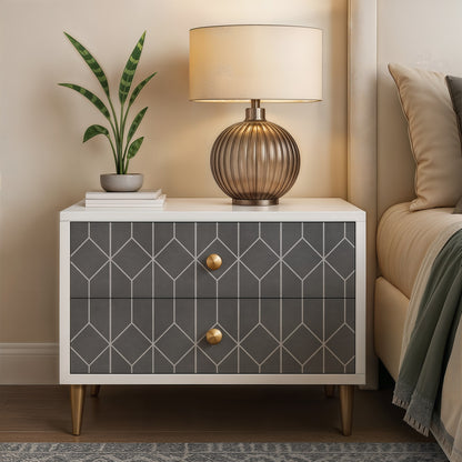 White nightstand with dark gray geometric doors, gold knobs and legs; ribbed bronze lamp, cream shade, books, snake plant.