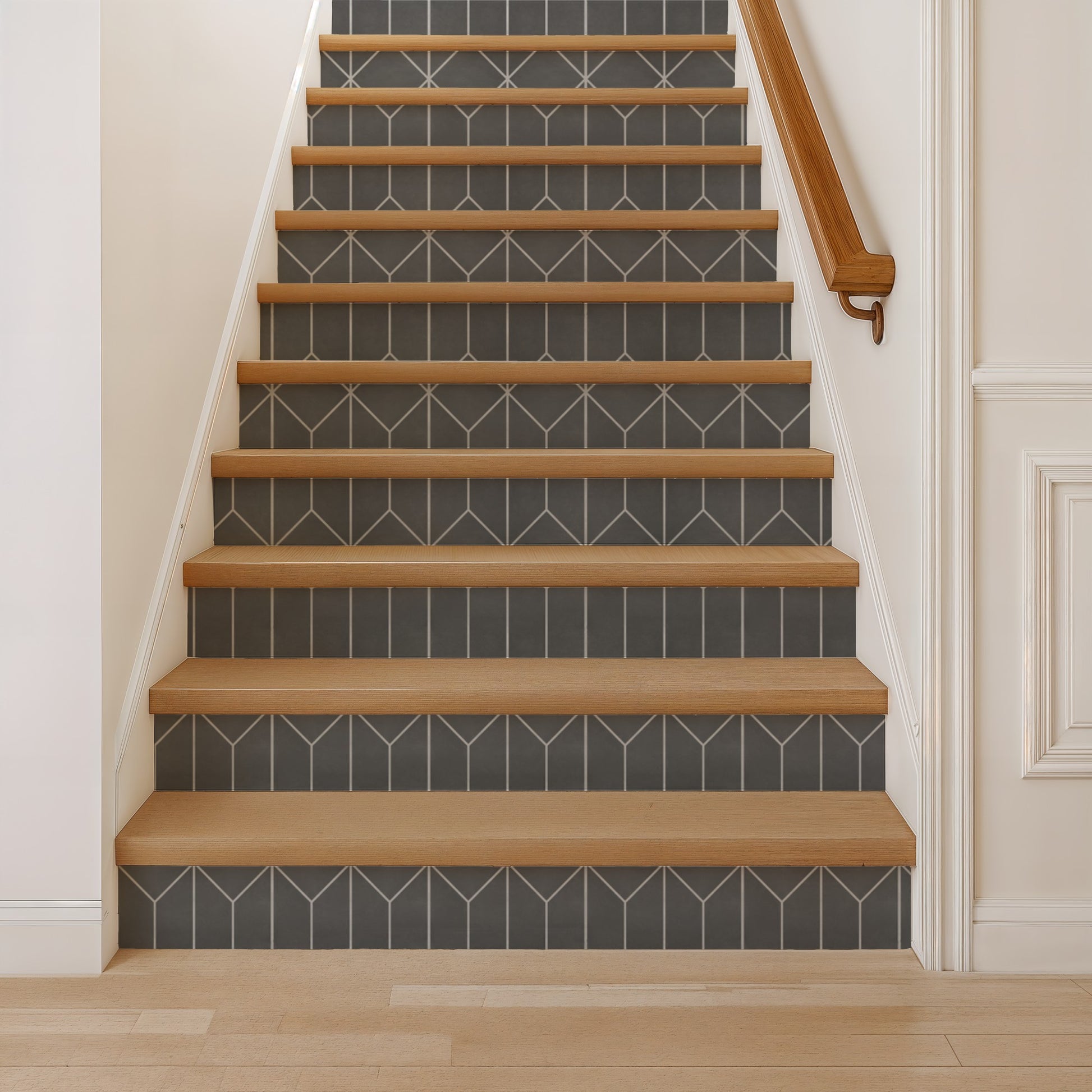 Wood stair treads with gray tile risers featuring white geometric chevrons, white walls, and a right-side wooden handrail.