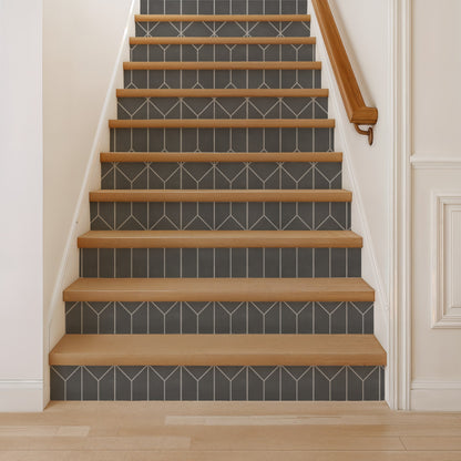 Wood stair treads with gray tile risers featuring white geometric chevrons, white walls, and a right-side wooden handrail.