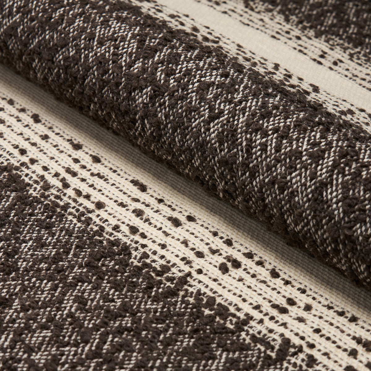 Dark brown and cream woven rug rolled up, with a textured striped pattern for rustic home decor.