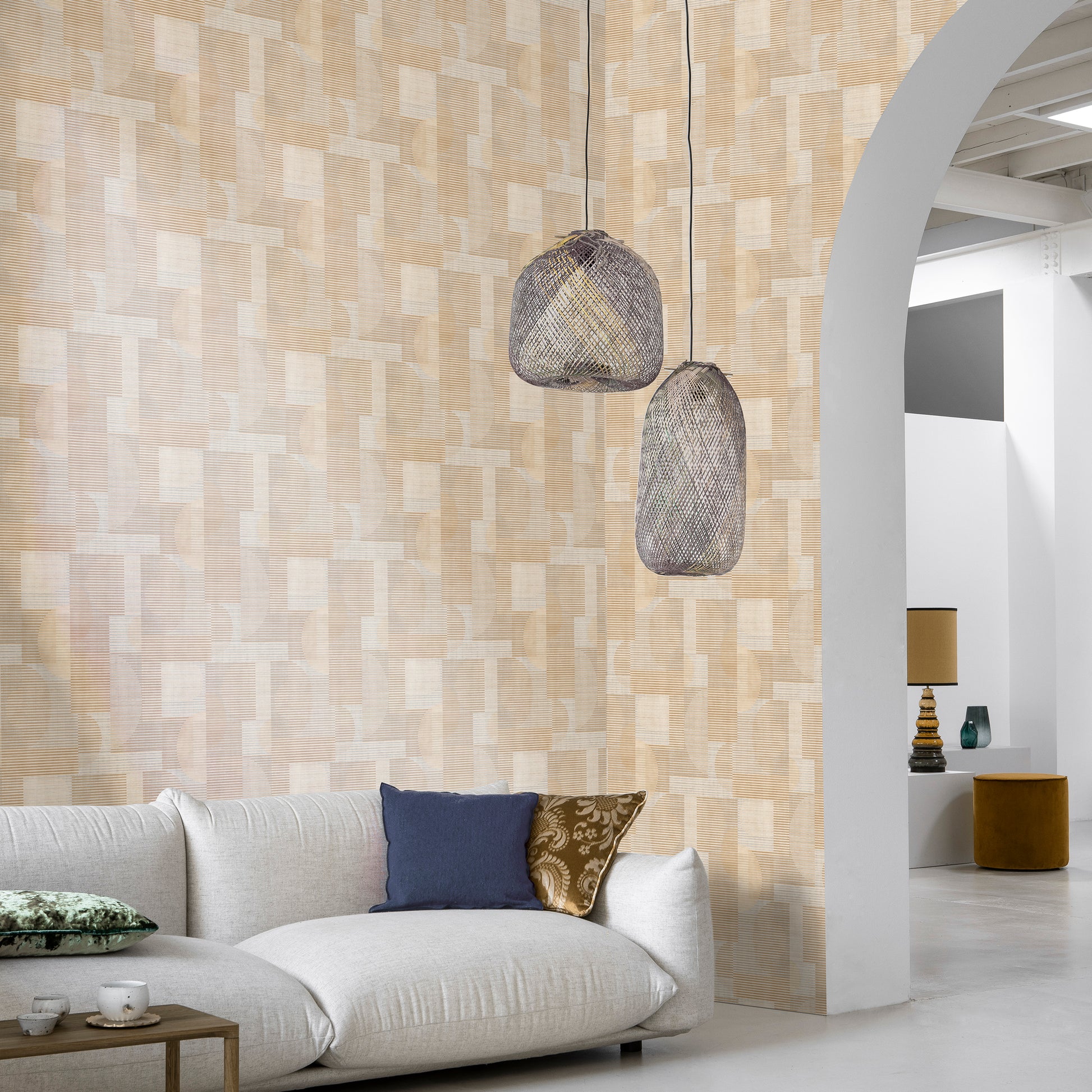 Living room with beige geometric wallpaper, white sofa, blue and brown cushions, and two woven rattan pendant lights.
