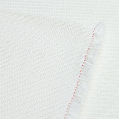 White woven textile with herringbone pattern, folded edge with red stitching and fringe detail.