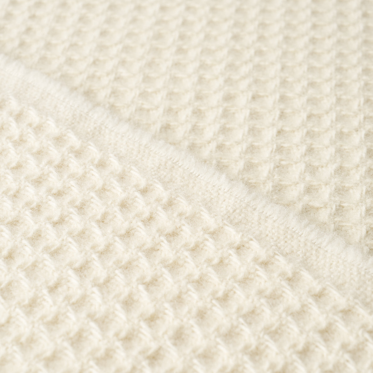Cream waffle-knit fabric close-up with diagonal fold, cozy soft knit texture.