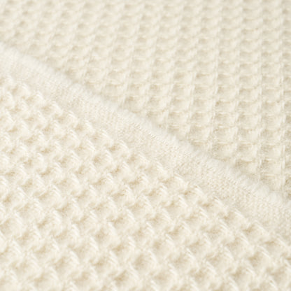 Cream waffle-knit fabric close-up with diagonal fold, cozy soft knit texture.