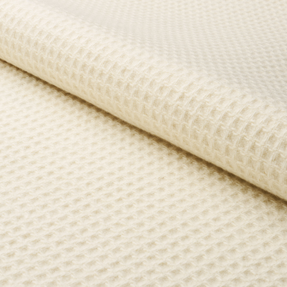 Cream waffle-knit fabric close-up with a folded edge; soft textured material for blankets, throws or cozy apparel.