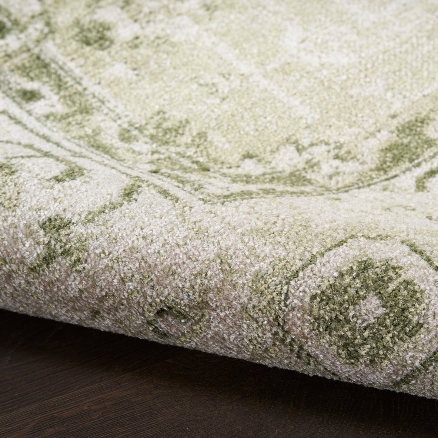 Olive green and beige oriental rug with medallion motif, thick plush pile, partially rolled edge on dark wood floor.