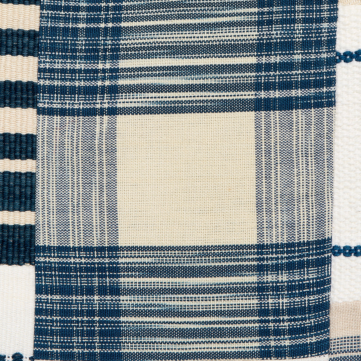 Close-up of woven patchwork fabric in indigo and cream with a large beige center square and striped borders.