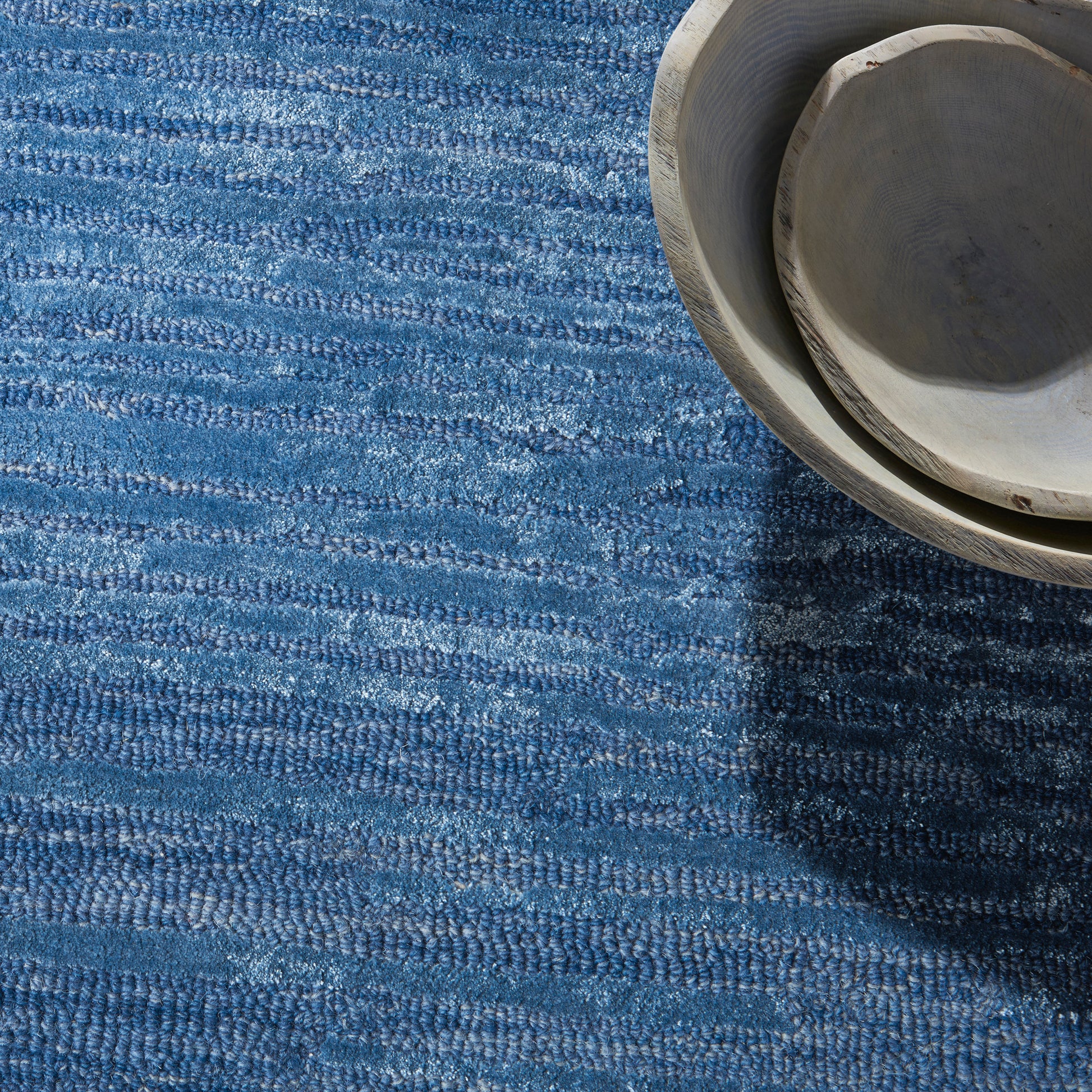 Blue woven area rug with a light gray ceramic bowl resting in the top-right corner of the rug.