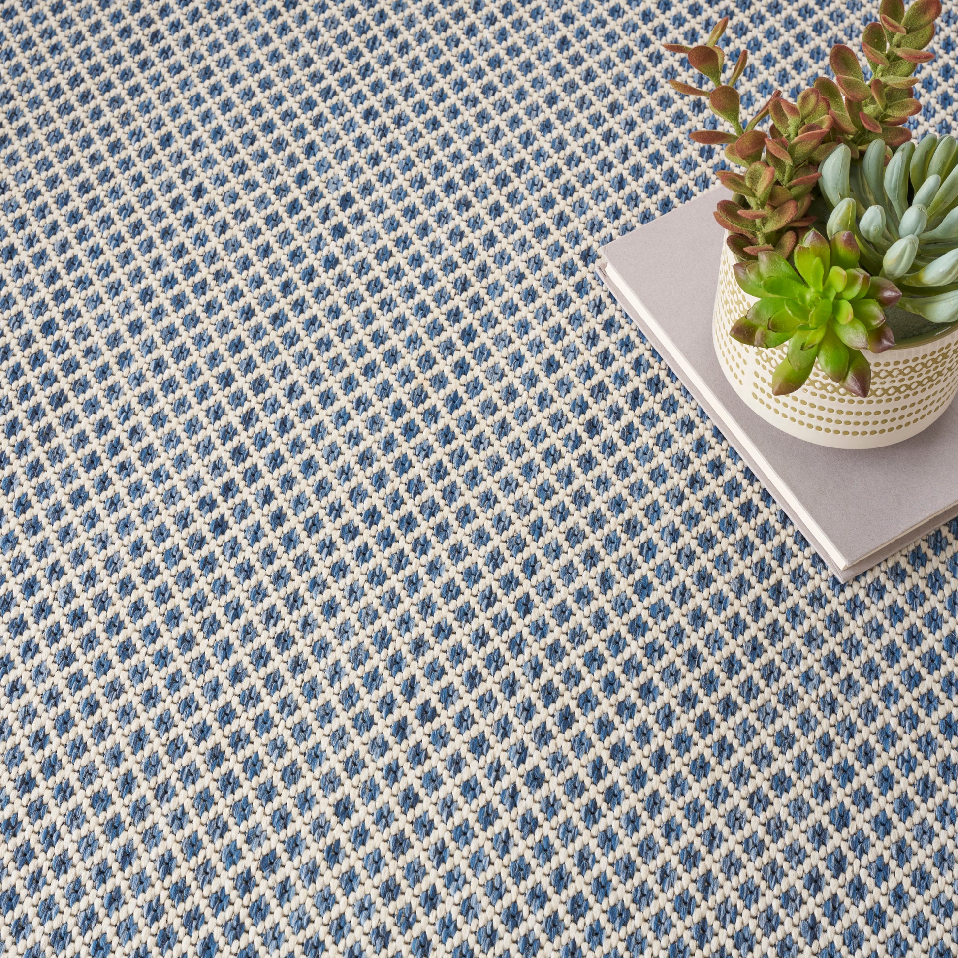 Large pale gray square panel dominates the frame; to the right a woven basket with succulents sits on a blue patterned rug.