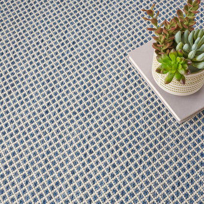 Large pale gray square panel dominates the frame; to the right a woven basket with succulents sits on a blue patterned rug.