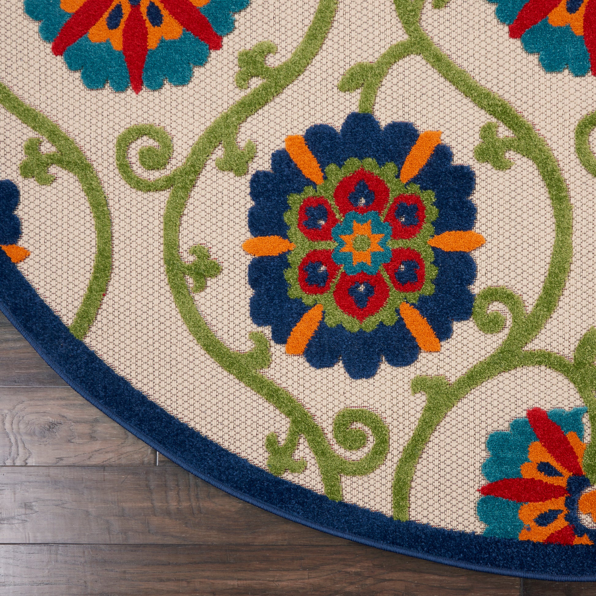 Round beige rug with blue border and vibrant multicolor floral medallions connected by green vines, on wood floor.