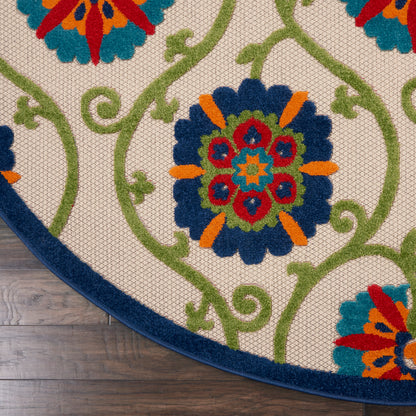 Round beige rug with blue border and vibrant multicolor floral medallions connected by green vines, on wood floor.