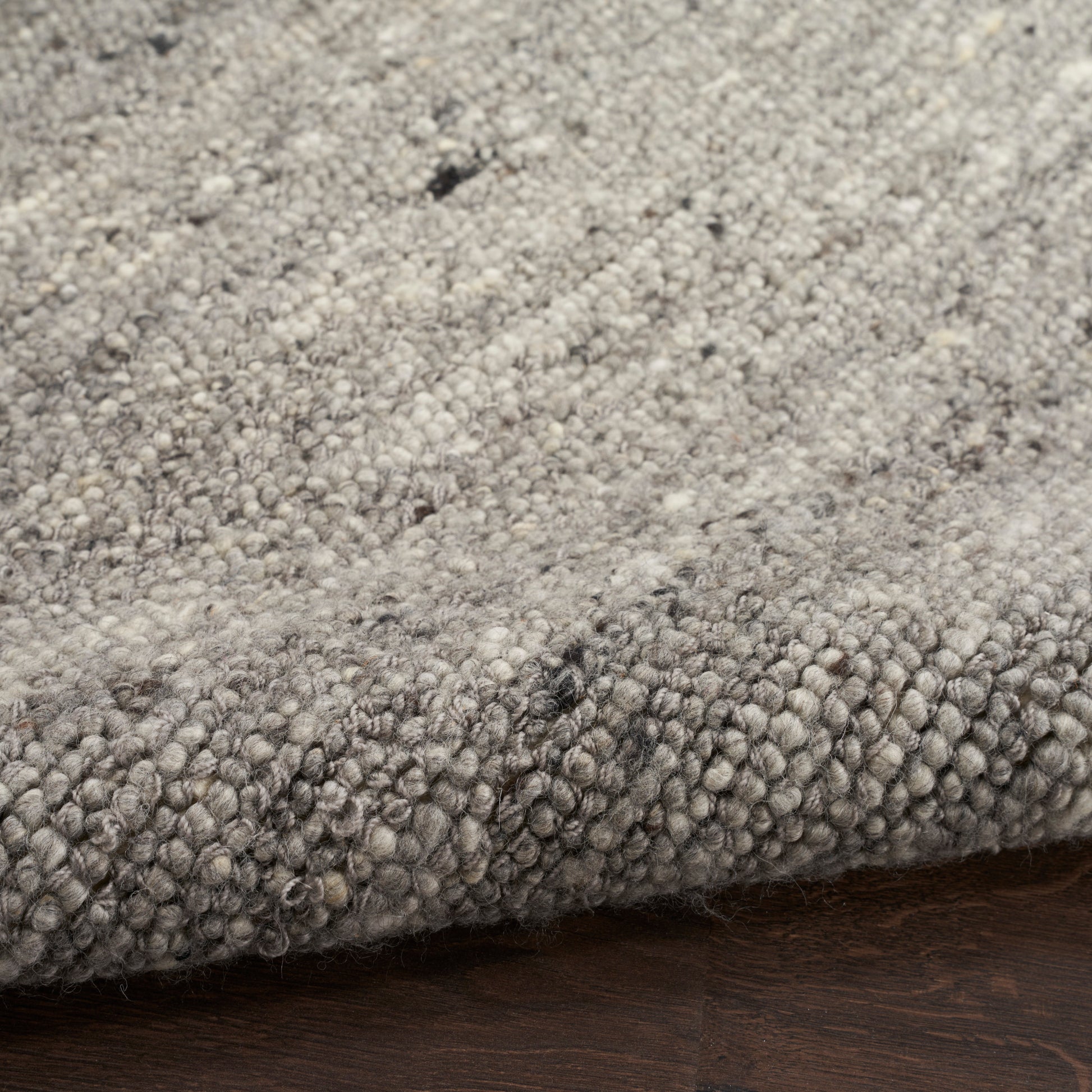Close-up of a dense grey loop-pile rug with mixed light and dark grey fibers on a wood floor.