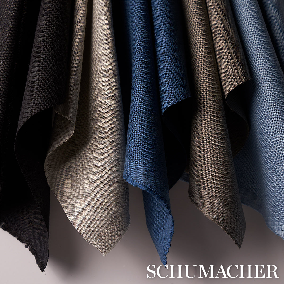 Hanging linen fabric swatches in black, beige, navy, gray and blue with frayed edges.