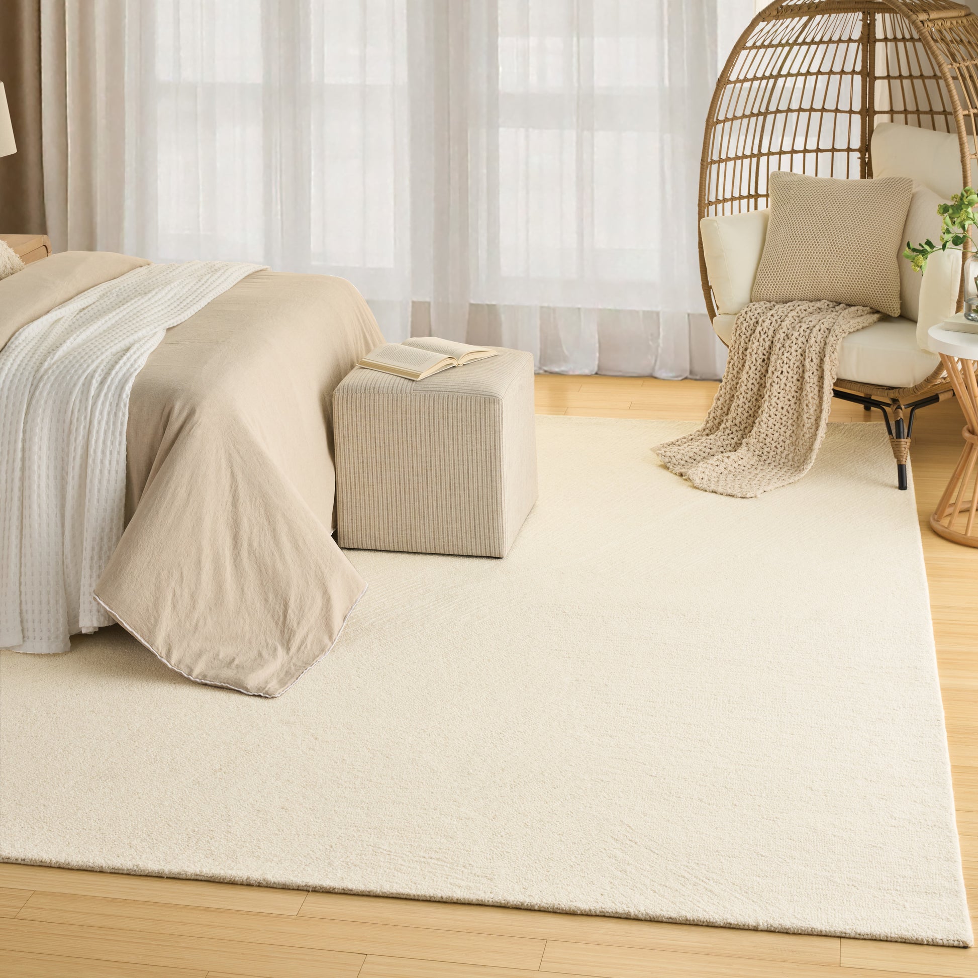 Bedroom with beige duvet on bed, cream area rug, light wood floor, wicker hanging chair, neutral cushions, cozy throw.