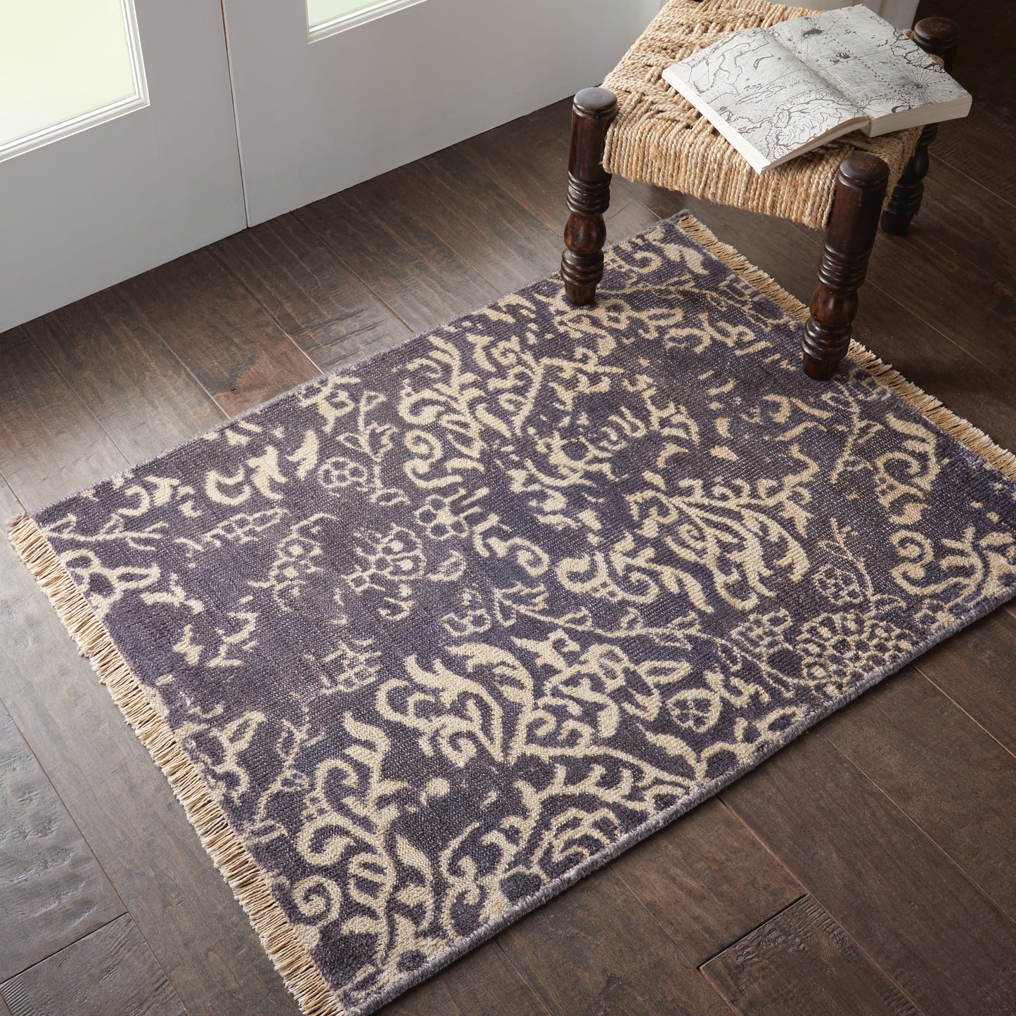Purple & cream arabesque patterned rug with fringed ends on a dark wood floor.